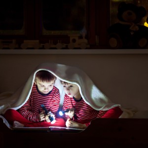Brothers reading under a blanket at night