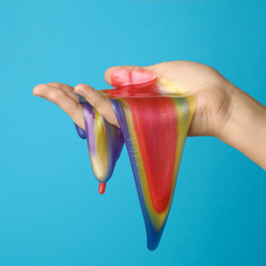 Hand holding rainbow slime against a blue background