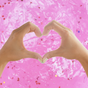 Hands making a heart shape over pink slime background