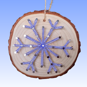 A wood slice with a snowflake on the surface, made out of string, against a blue background