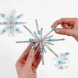 A silver snowflake made of pipe cleaners and beads against a soft white background.