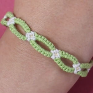 A dainty green and white friendship bracelet on someone's wrist.
